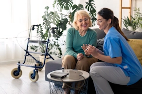 Life Assure Senior Woman Sitting In Chair And Laughing With Caregiver Nurse Blog